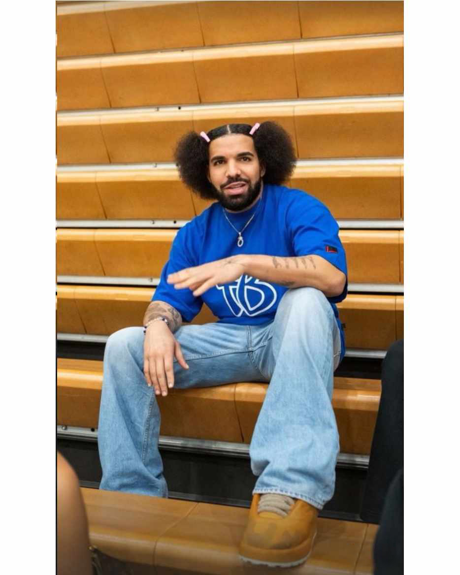 Drake wears pink hairclips, a blue Fubu T-shirt, baggy jeans & chunky sneakers